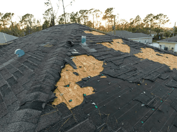 Storm-damaged roof with sections of shingles torn away, exposing the bare roof deck underneath