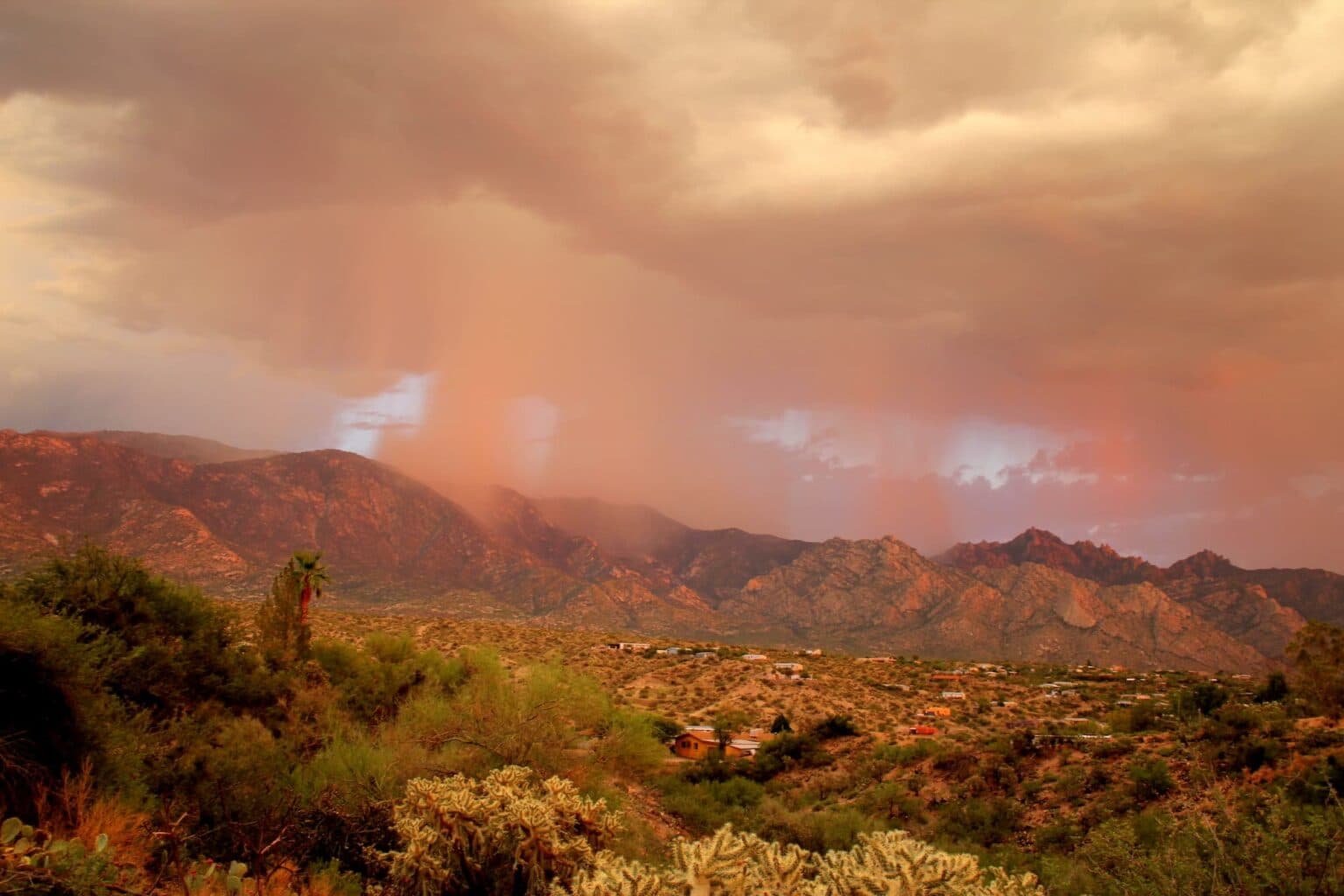 Monsoon rain sweeping across Arizona desert mountains above a hillside neighborhood at sunset