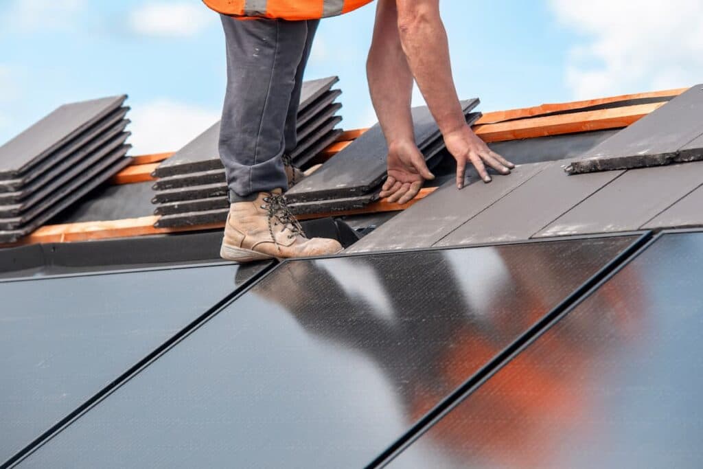 Roofer laying flat roof tiles alongside a row of rooftop solar panels