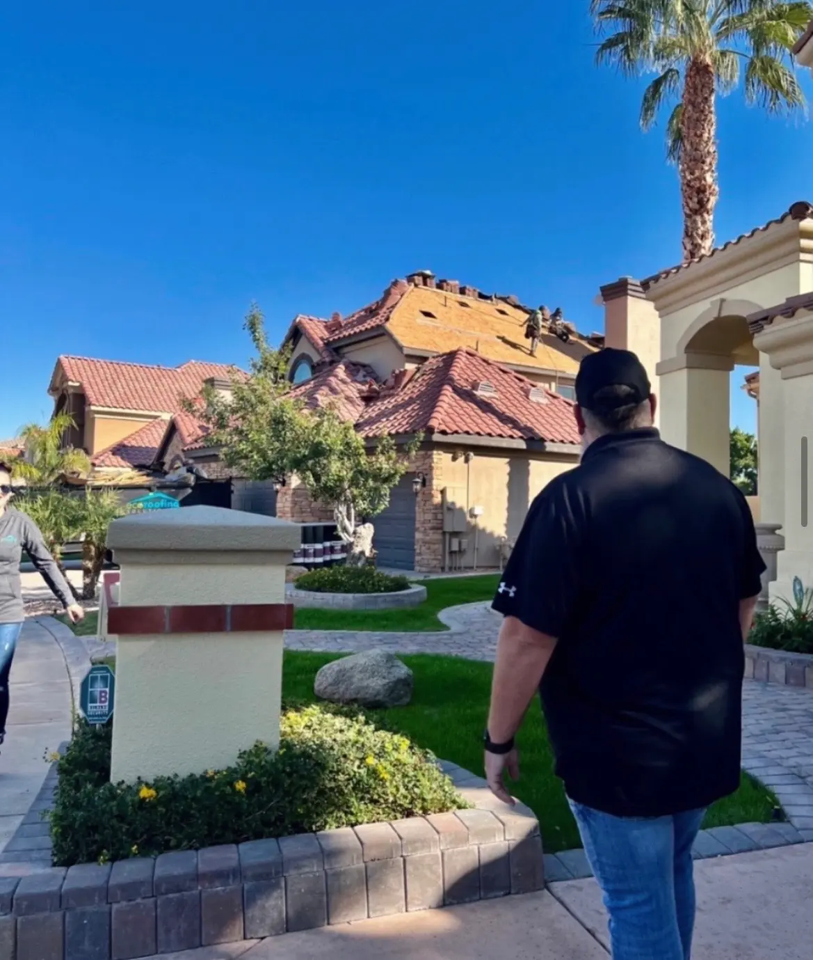 Eco Roofing Solutions crew re-roofing a tiled Arizona home while a team member walks up the driveway