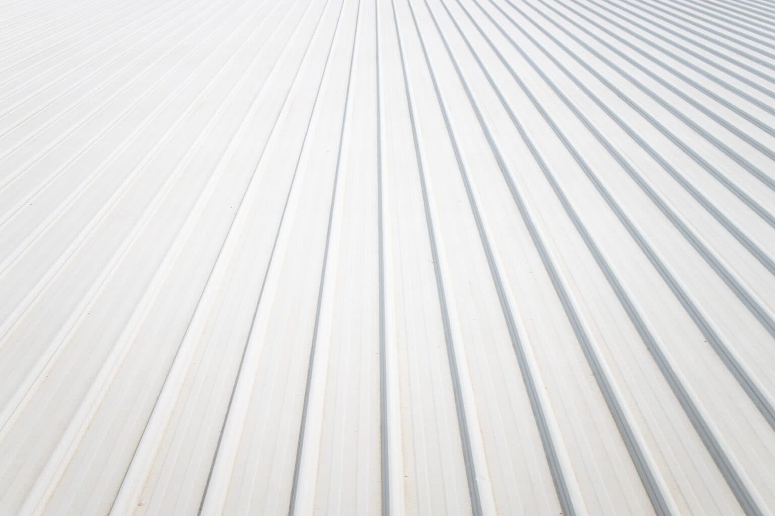 Close-up of a bright white ribbed metal roof reflecting the sun