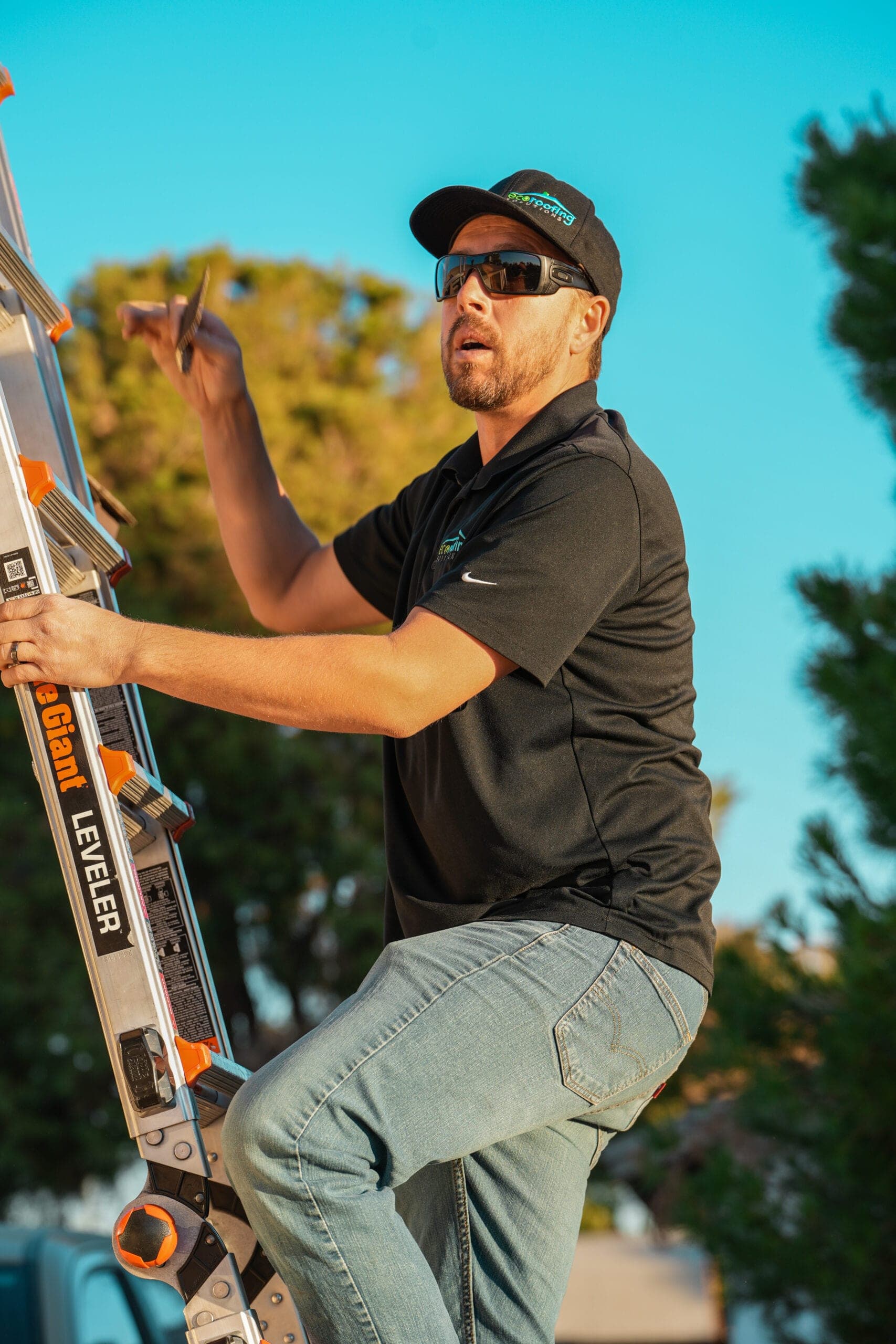 Eco Roofing Solutions team member on a ladder inspecting a shingle in the Arizona sun