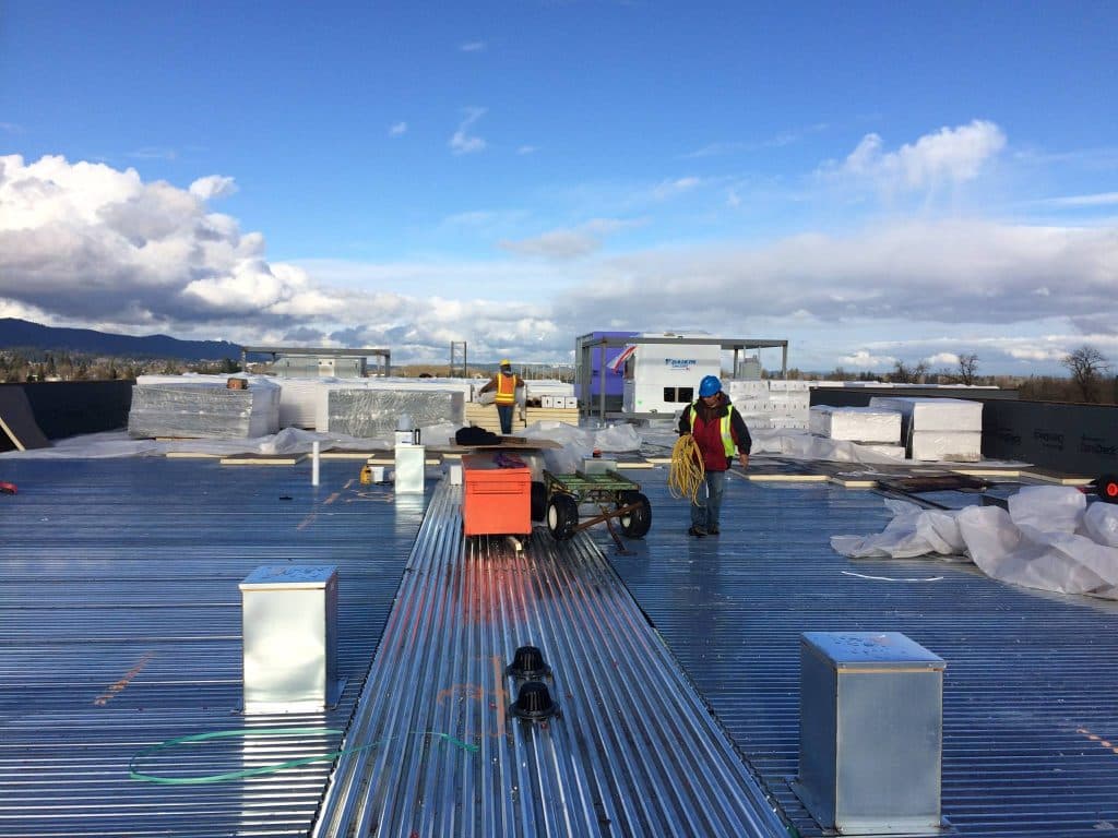 Crew staging insulation board across a commercial metal roof deck
