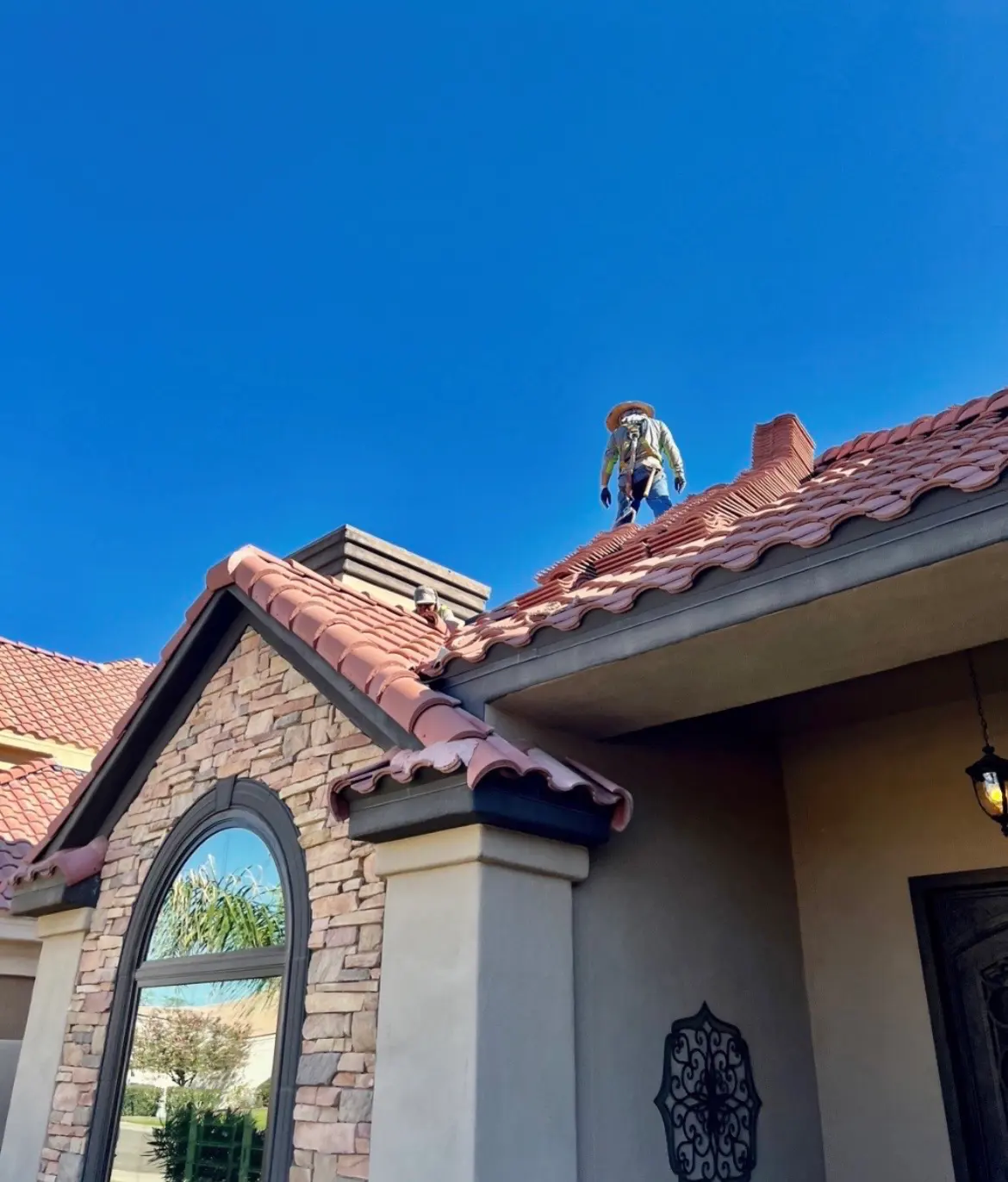 Roofers setting clay barrel tile along the ridge of a home under a clear desert sky
