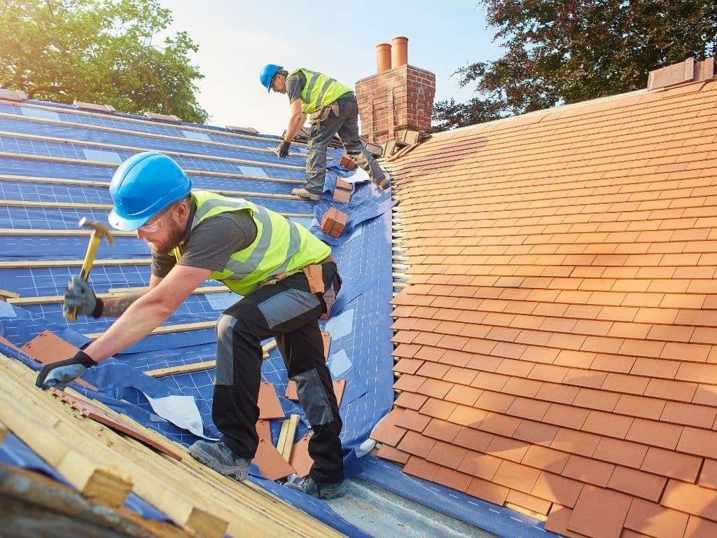 Roofers fastening tile over fresh underlayment during a roof replacement