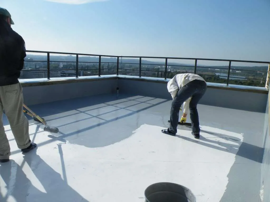 Two roofers rolling a reflective waterproof coating across a low-slope rooftop